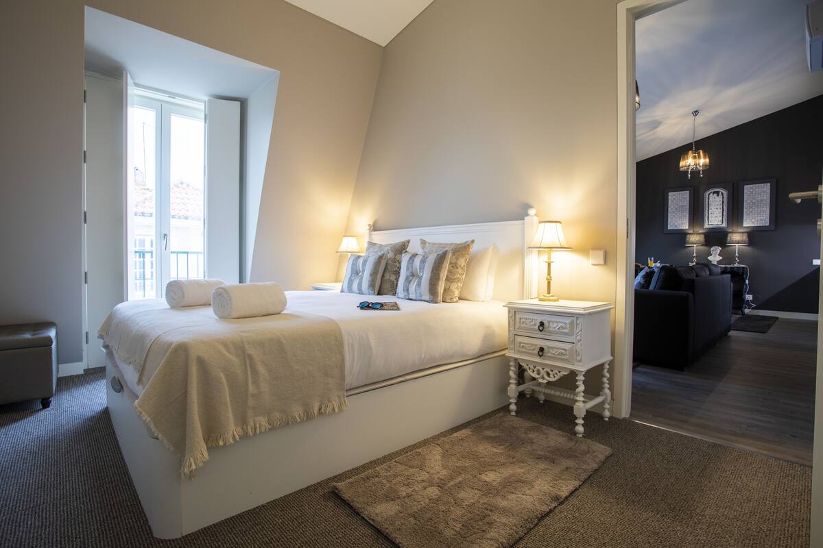 A bedroom with a large bed, bedside lamps, a small bedside table, and a view of a balcony.