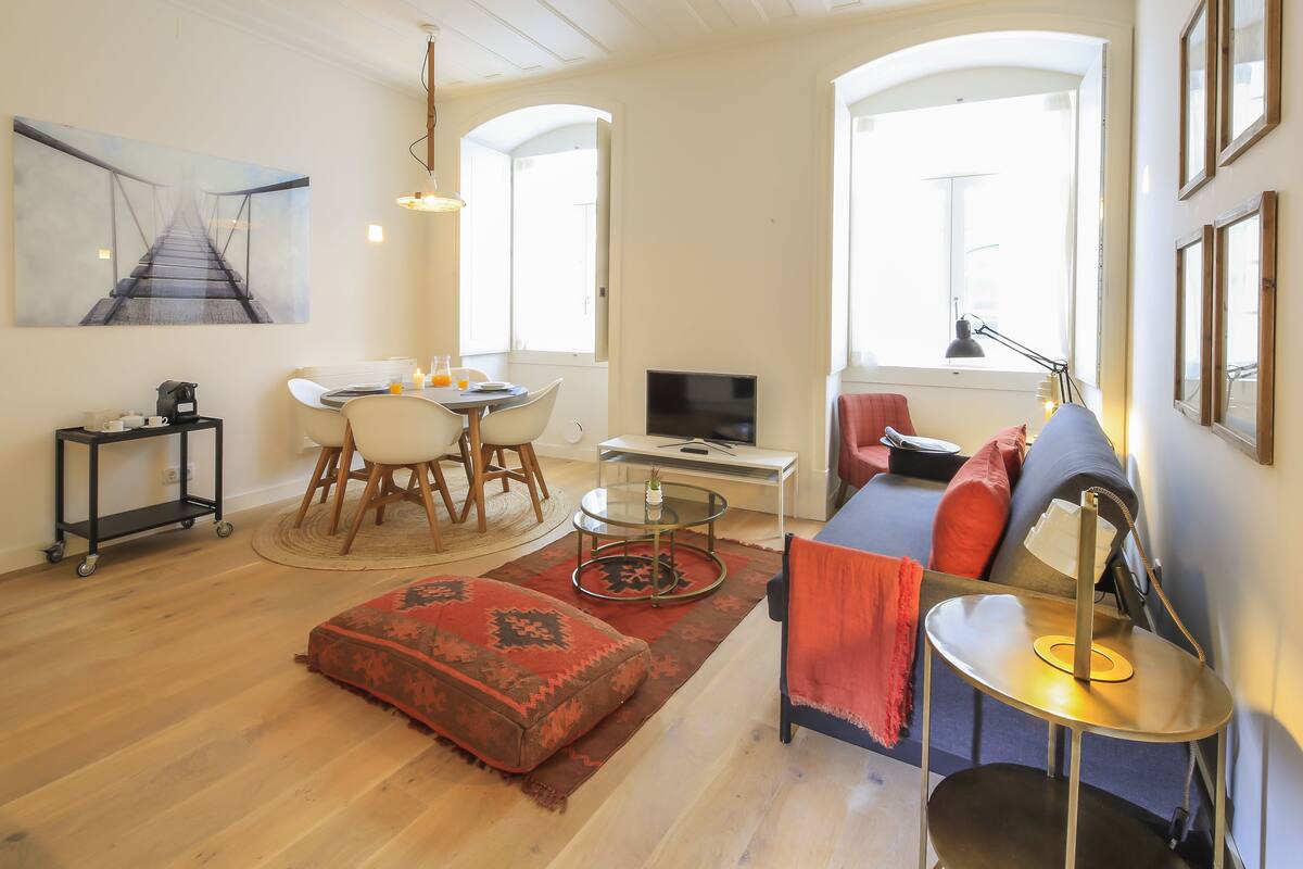 A living room with a sofa, a coffee table, a TV, and a dining area with chairs and a table.