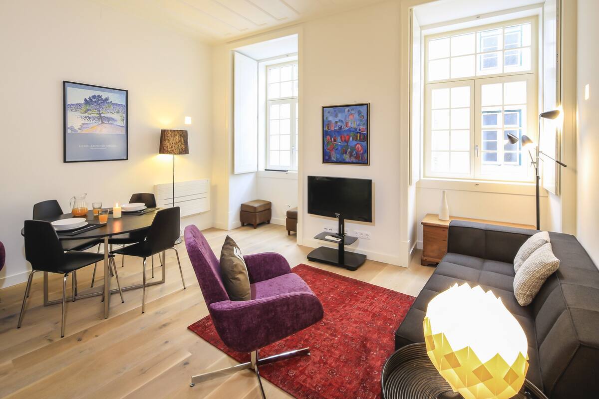 A modern living room with a dining area, a sofa, a TV, and artwork on the walls.