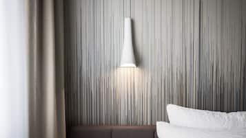 A modern hotel room with a textured wall, a white lamp, and a bed with white linens.