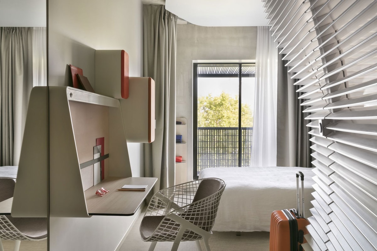 Una habitación de hotel moderna con cama, escritorio, sillas y un balcón con vistas.