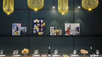 A dining area with a long table set for a meal, featuring hanging yellow pendant lights and artwork on the wall.