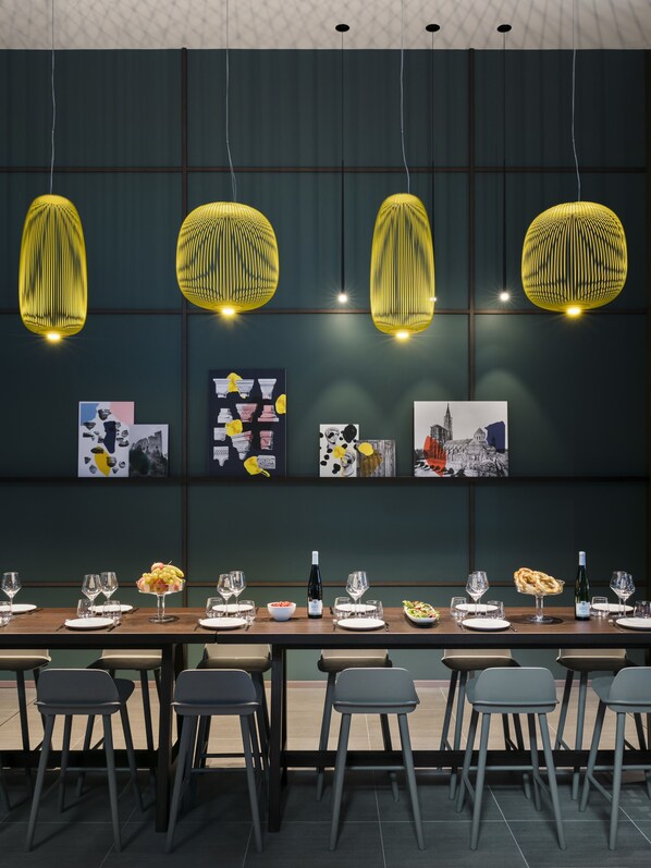 Un comedor con una mesa larga dispuesta para una comida, con lámparas colgantes amarillas y obras de arte en la pared.