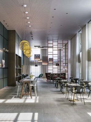 A modern interior with a dining area, high ceilings, and a mix of natural and artificial lighting. - OKKO Hotels Strasbourg Centre (Strasbourg)