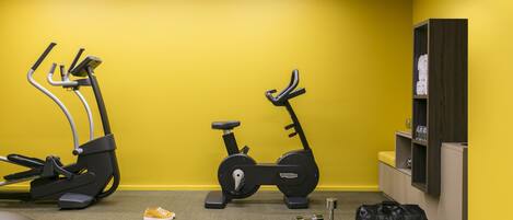 A gym with two exercise bikes and a treadmill, a yoga mat, and a black bag on the floor.