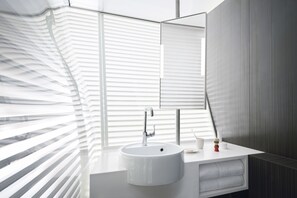 A modern bathroom with a white sink, a mirror, and a window with blinds. - OKKO Hotels Strasbourg Centre (Strasbourg)