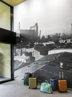 A wall with a black and white photo of a harbor, luggage, and a window with a black frame. - OKKO Hotels Strasbourg Centre (Strasbourg)