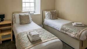 A hotel room with two beds, a bedside table, a lamp, and a window. - The Boyne Hotel (Banff)