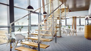 A modern interior with a wooden staircase, glass walls, and a view of the ocean.