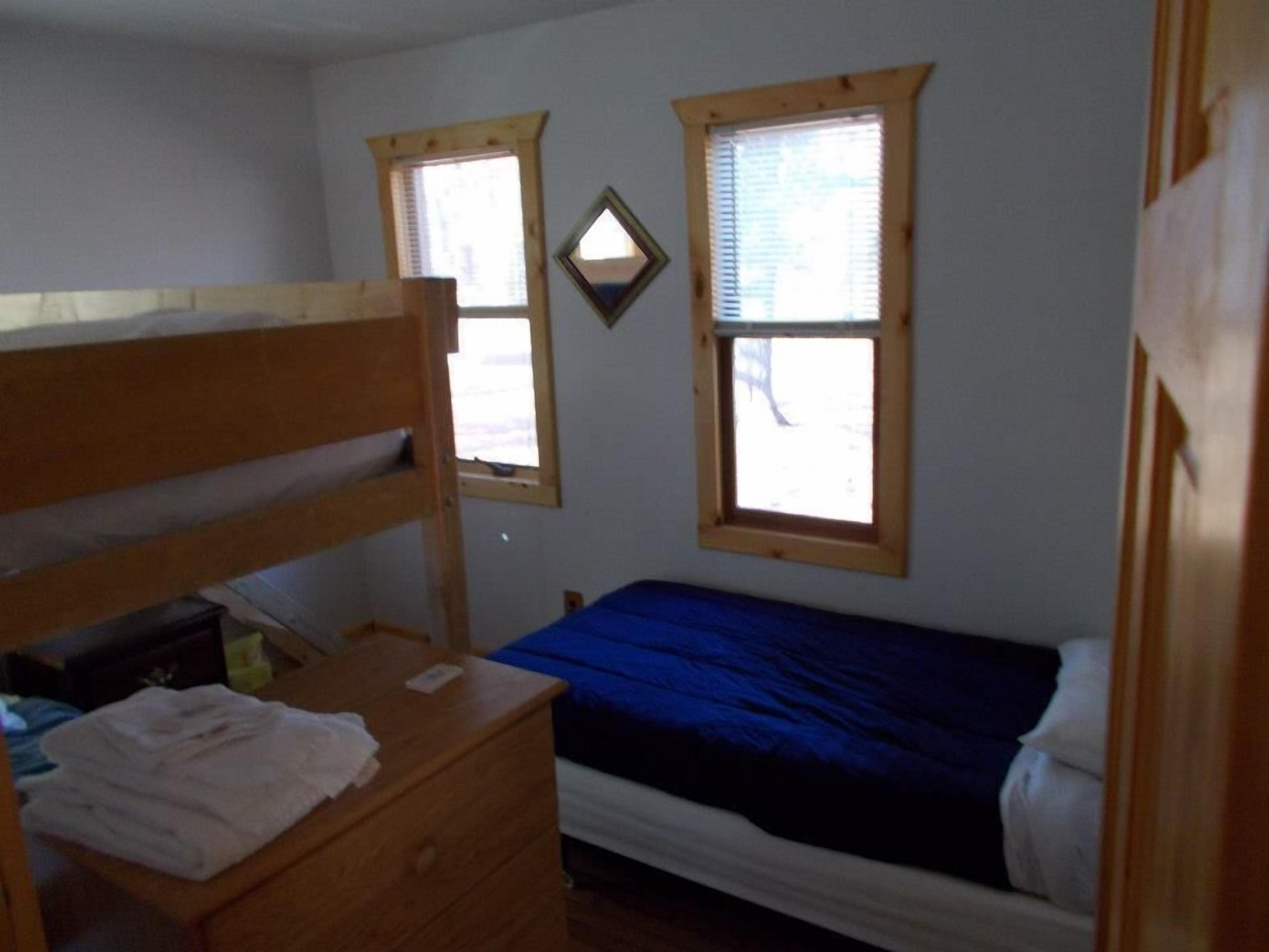A bedroom with a bunk bed, a single bed, wooden windows, and a small dresser.