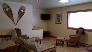 Una sala de estar con sofá, sillas, televisor y ventana.