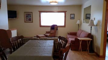 Un coin repas avec une table et des chaises, une fenêtre donnant sur un beau paysage, un canapé, un fauteuil et une lampe.