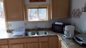 Una cocina con armarios de madera, una ventana, un lavamanos, un microondas y una cafetera.
