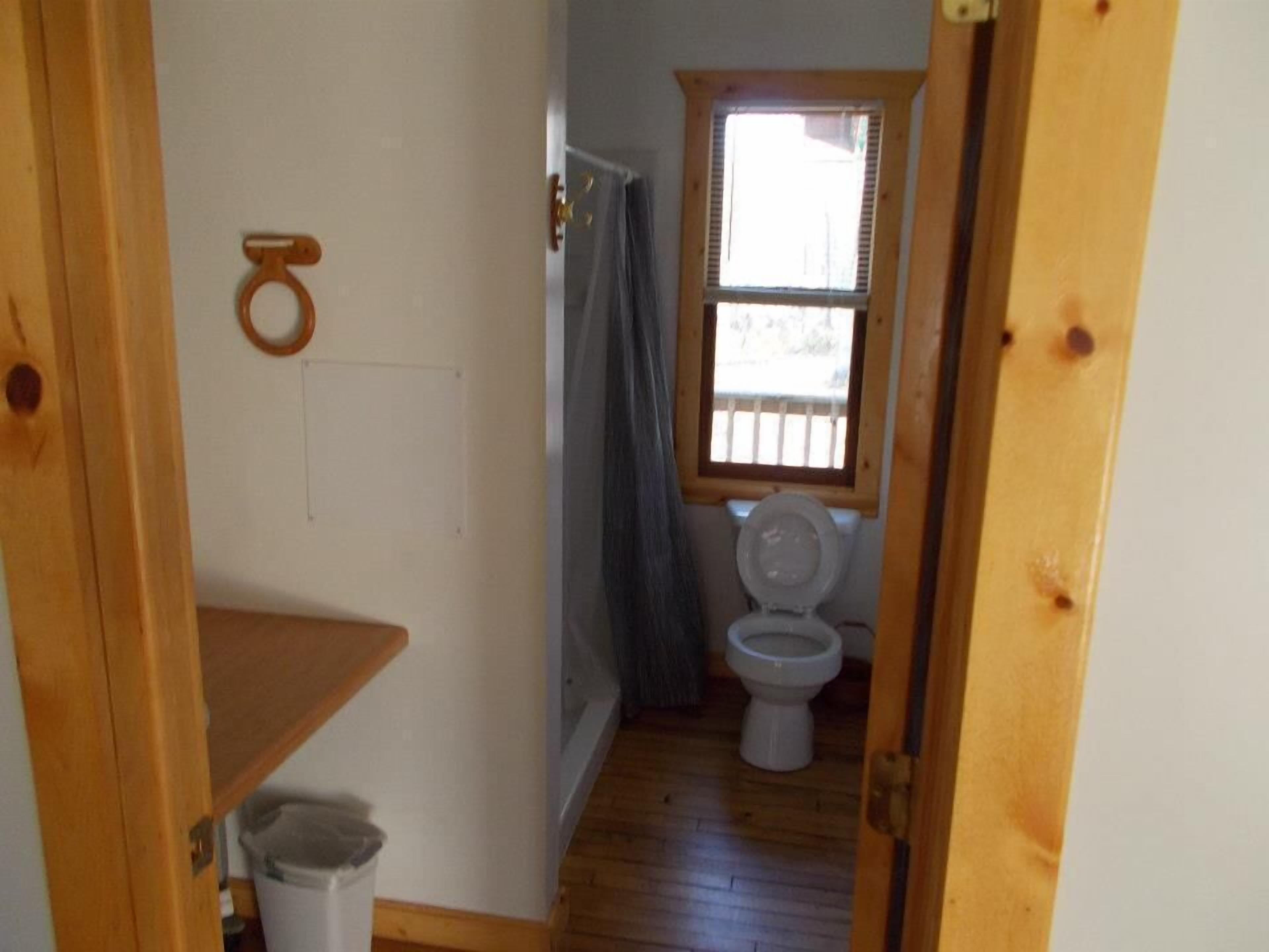 Une petite salle de bain étroite, avec un plancher en bois, des toilettes blanches et une fenêtre à cadre en bois.