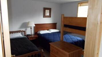 A room with two beds, a wooden dresser, a nightstand with a lamp, and a framed picture on the wall.