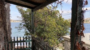 A covered outdoor area with a view of a body of water, a wooden fence, and greenery. - Yali Butik Pansiyon (Karaburun)