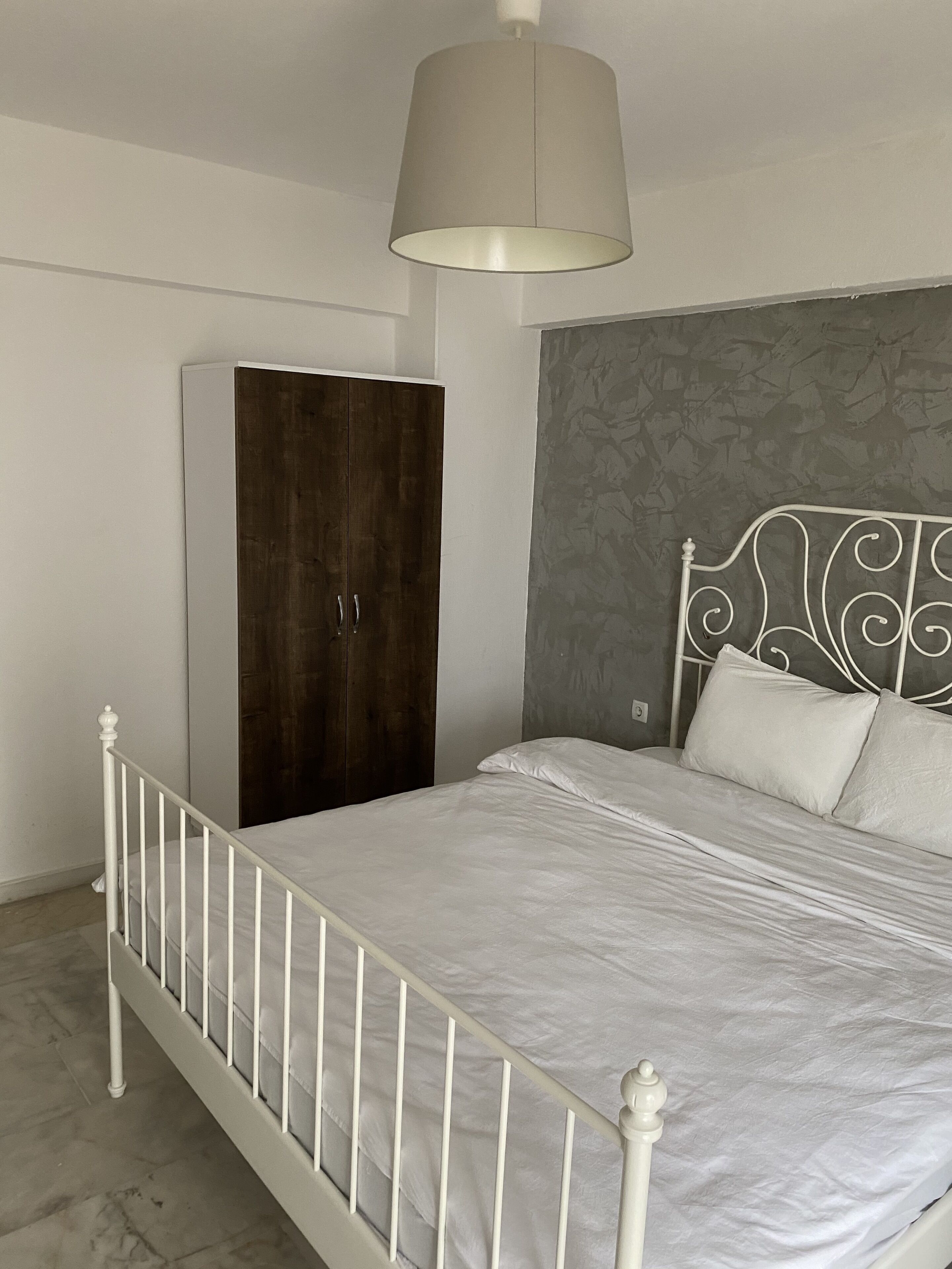 A bedroom with a white metal bed frame, a dark wooden wardrobe, and a grey patterned headboard.