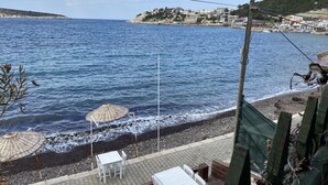 A coastal view with a beach, umbrellas, and tables. - Yali Butik Pansiyon (Karaburun)