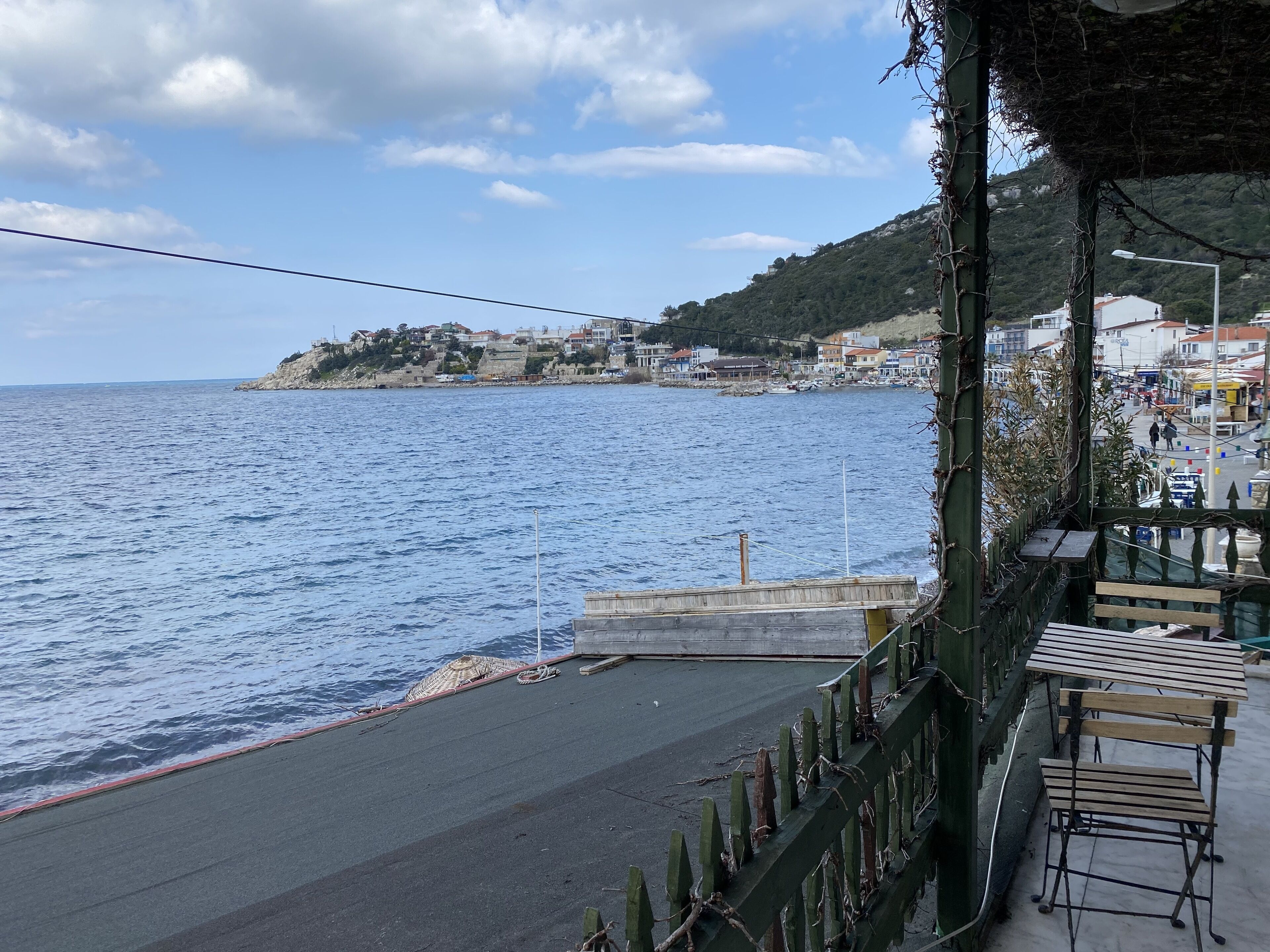 A coastal view with a pier extending into the sea, a small dock with a boat, and a town with buildings in the background.