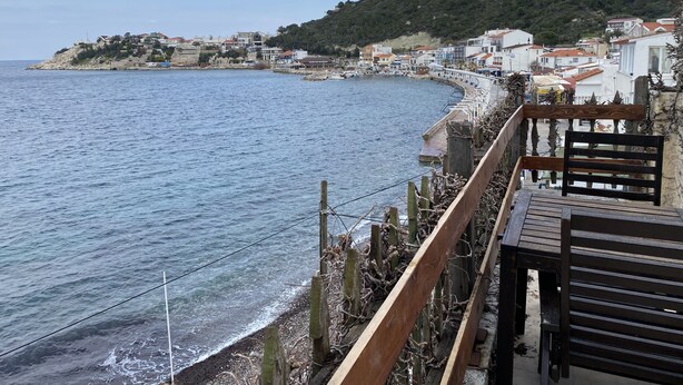 A coastal town with a wooden walkway overlooking the sea, buildings along the shore, and a hill in the background. - Yali Butik Pansiyon (Karaburun)