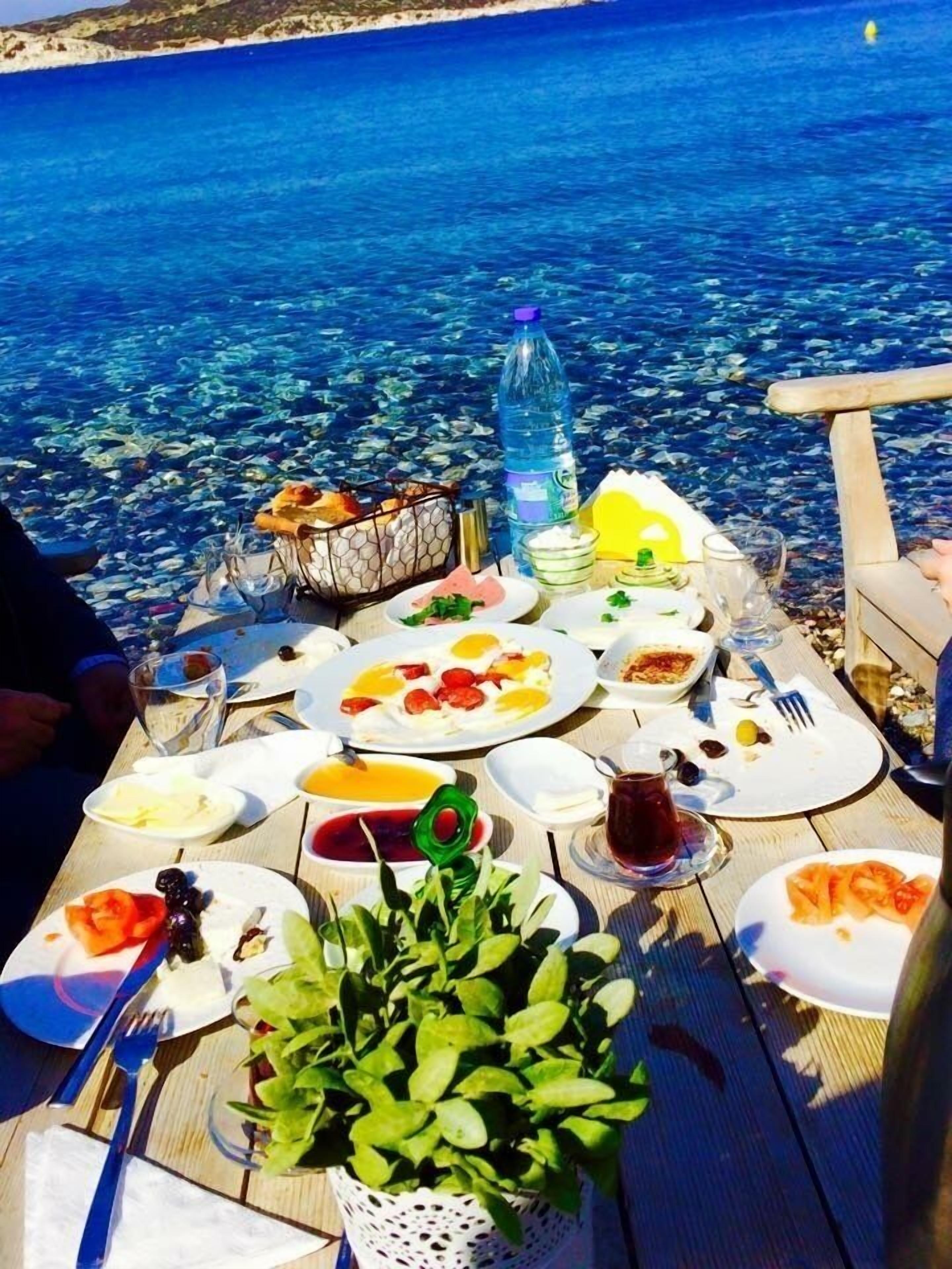 A table set with breakfast items and a bottle of water, overlooking a clear blue sea.