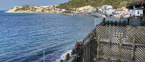 A coastal view with a wooden fence, a paved walkway, and a hillside with buildings.
