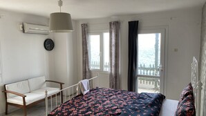 A bedroom with a bed, a chair, a window with curtains, and a view of the sea. - Yali Butik Pansiyon (Karaburun)