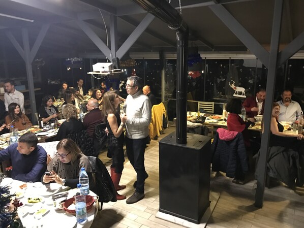 An outdoor dining area with tables and chairs, a large black heater, and a glass enclosure with a view of the night sky. - Yali Butik Pansiyon (Karaburun)