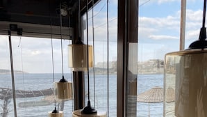A room with large windows overlooking the sea, featuring multiple hanging lamps and a wooden table with a potted plant. - Yali Butik Pansiyon (Karaburun)