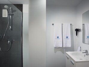 Un baño moderno con cabina de ducha de vidrio, un lavamanos blanco y dos toallas colgadas en ganchos.