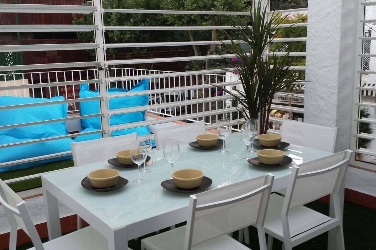 Un comedor con una mesa preparada para cuatro personas, rodeada de sillas blancas.