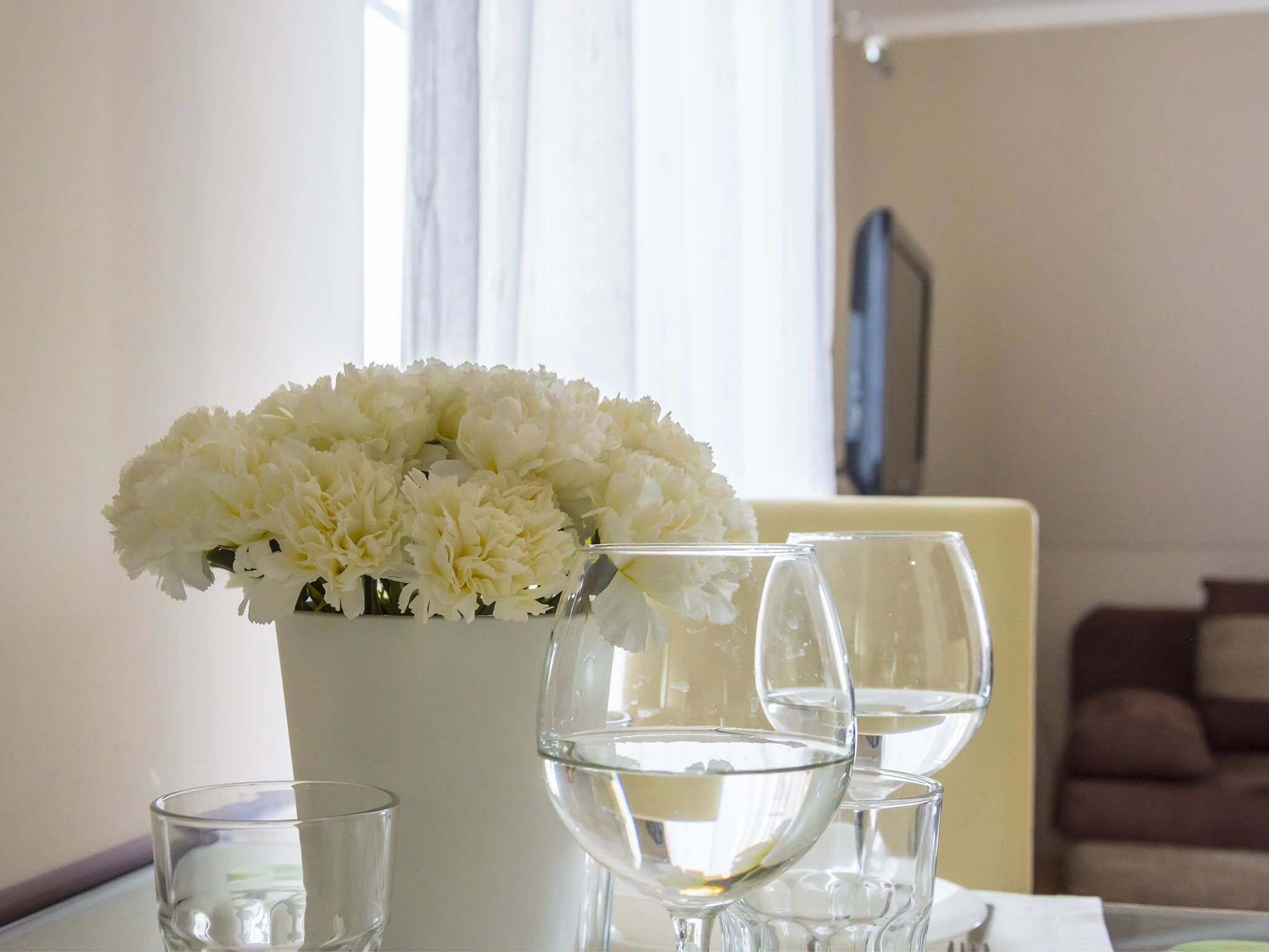 A table with a vase of white flowers and three clear glasses of water.