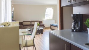 A modern kitchen with a Bosch coffee maker, a dining area with a glass table and chairs, a sofa, and a window with a view.