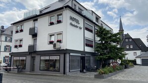 Un hotel con fachada moderna, varias ventanas con jardineras y una entrada visible con un cartel.