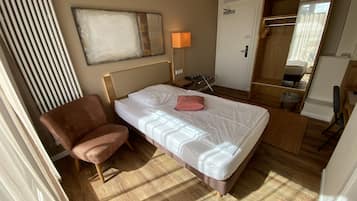 A hotel room with a bed, a chair, a lamp, a wardrobe, and a mirror.