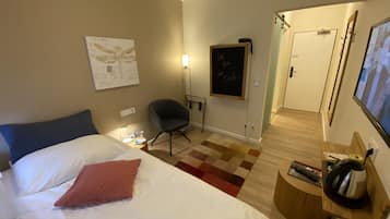 Una habitación de hotel con cama, una silla, un escritorio con computadora, teléfono en la pared y una puerta.