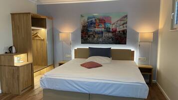 A modern hotel room with a large bed, wooden wardrobe, bedside lamps, and a cityscape painting on the wall.