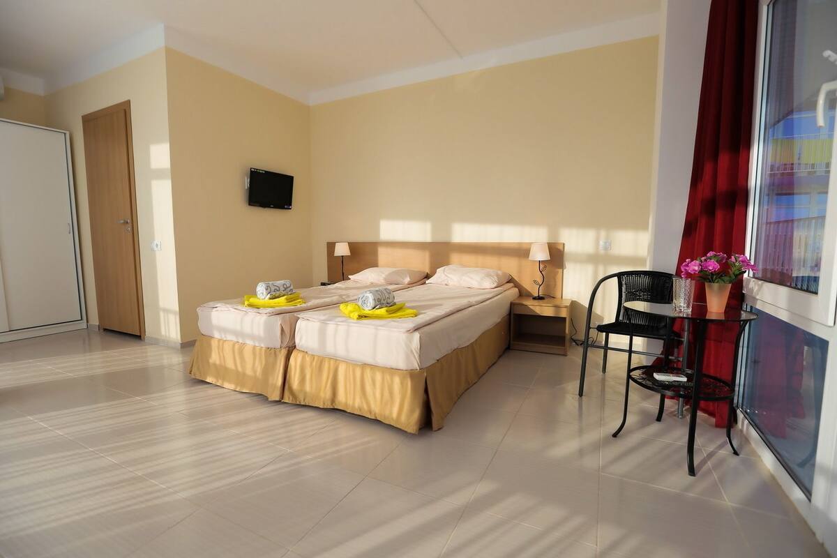 A hotel room with two beds, a TV, a desk with a chair, and a window with curtains.