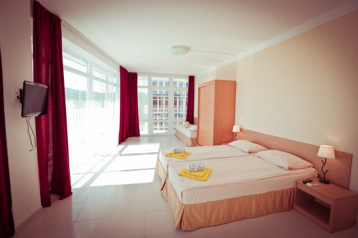 A hotel room with a bed, bedside tables, a TV, and a view of the outside.