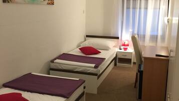 A room with two single beds, a desk, a chair, a small table, and a painting of a beach scene.