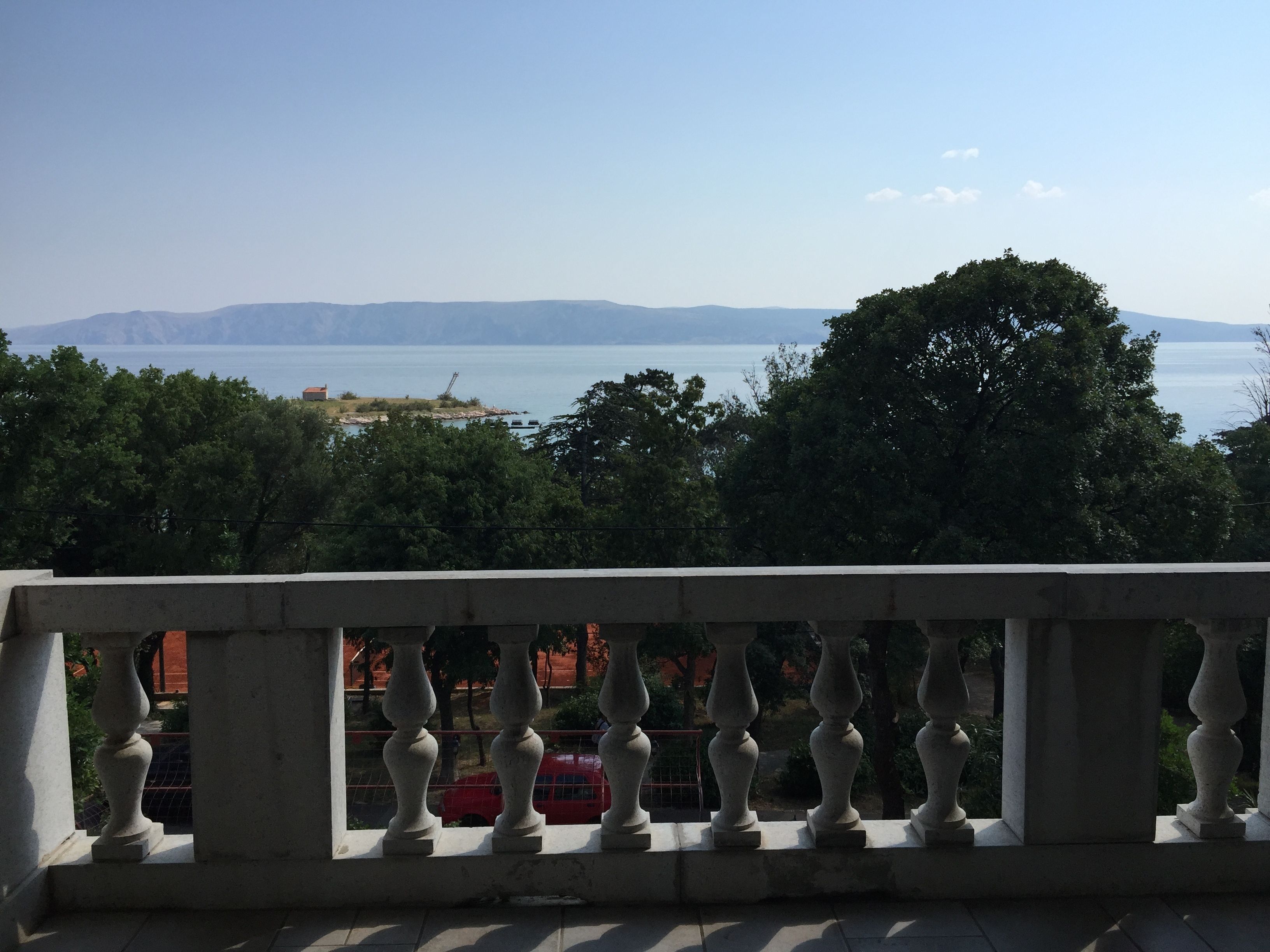 A balcony with a balustrade overlooking a body of water and distant mountains.