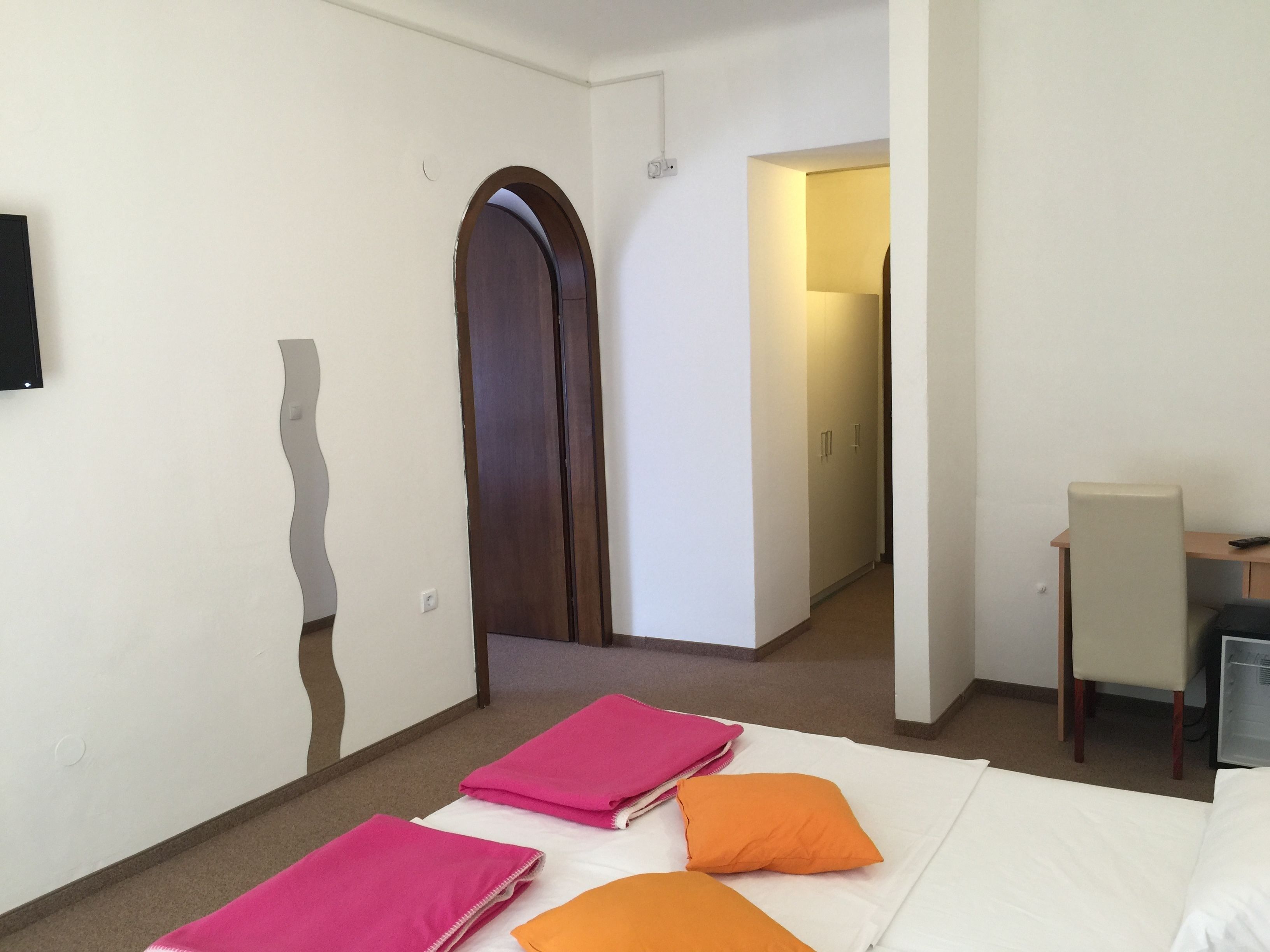 Ein Hotelzimmer mit einem Bett, einem Schreibtisch und einem Stuhl. Eine Tür führt in einen weiteren Raum.