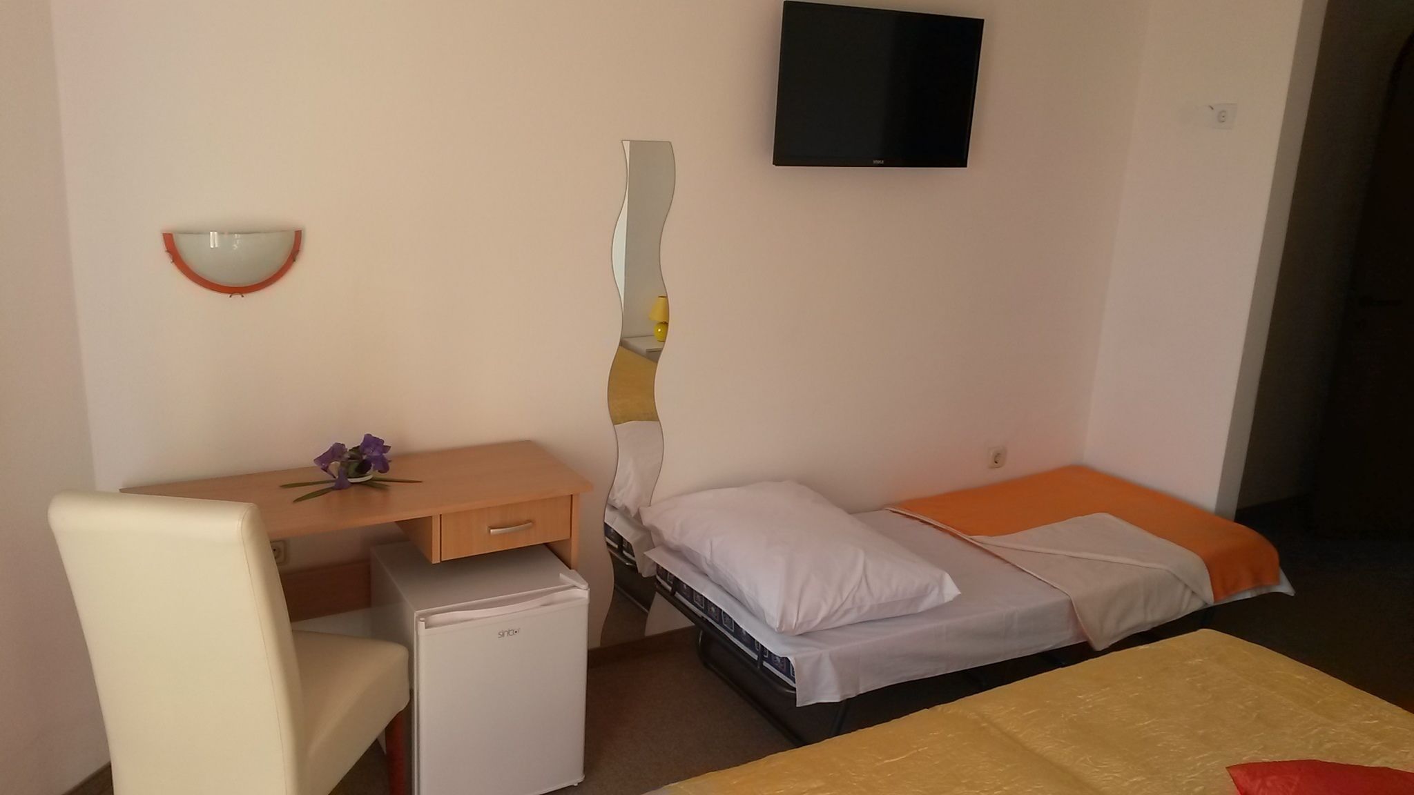 A compact room with a bed, a desk, a chair, and a small refrigerator.
