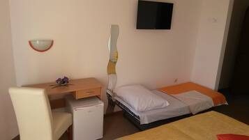 A compact room with a bed, a desk, a chair, and a small refrigerator.