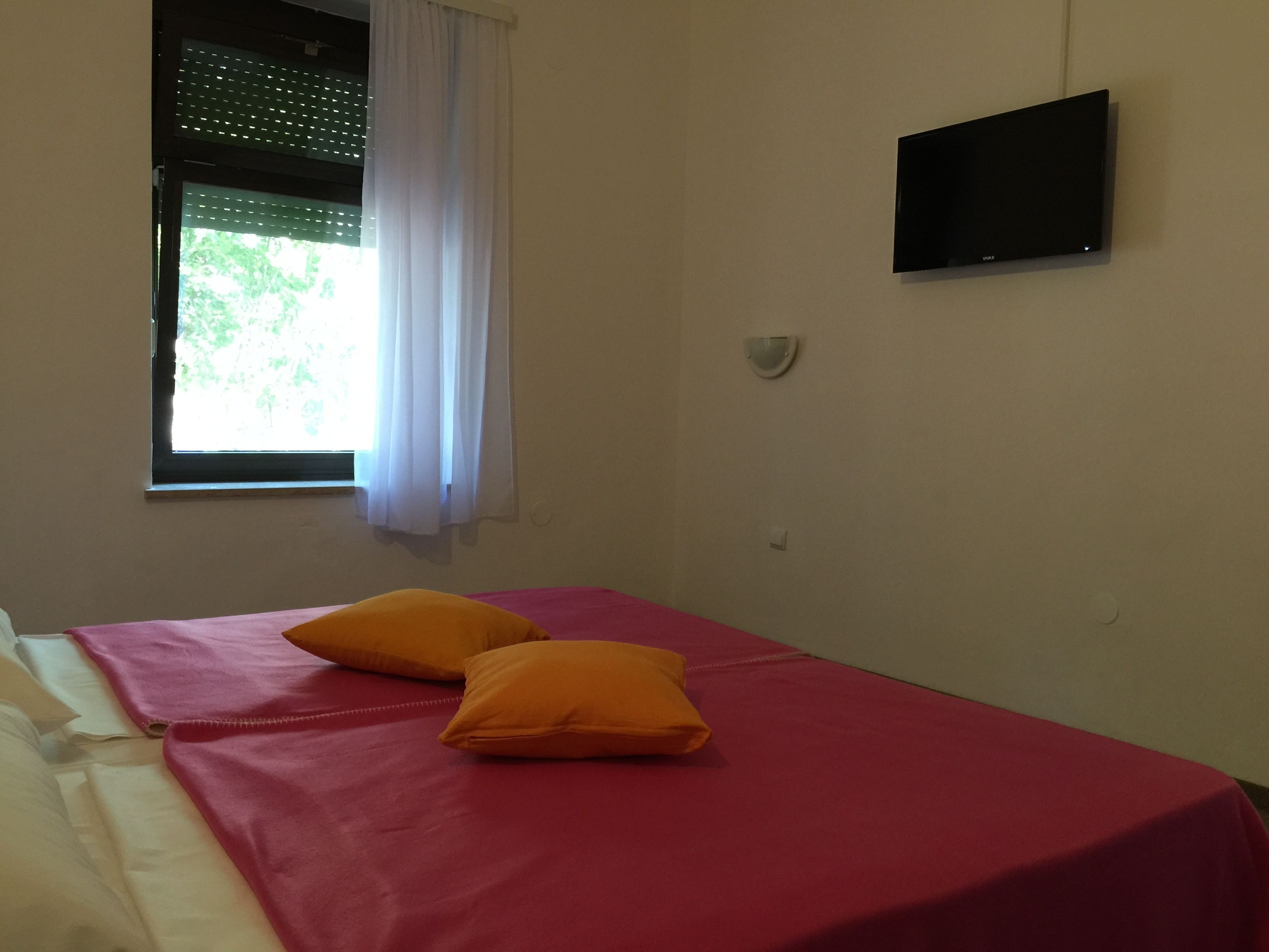 A room with a bed, a window with curtains, a wall-mounted TV, and a wall socket.
