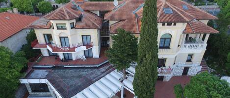 Un edificio grande de varios pisos con techo de tejas rojas, varios balcones y un patio con mesas al aire libre.