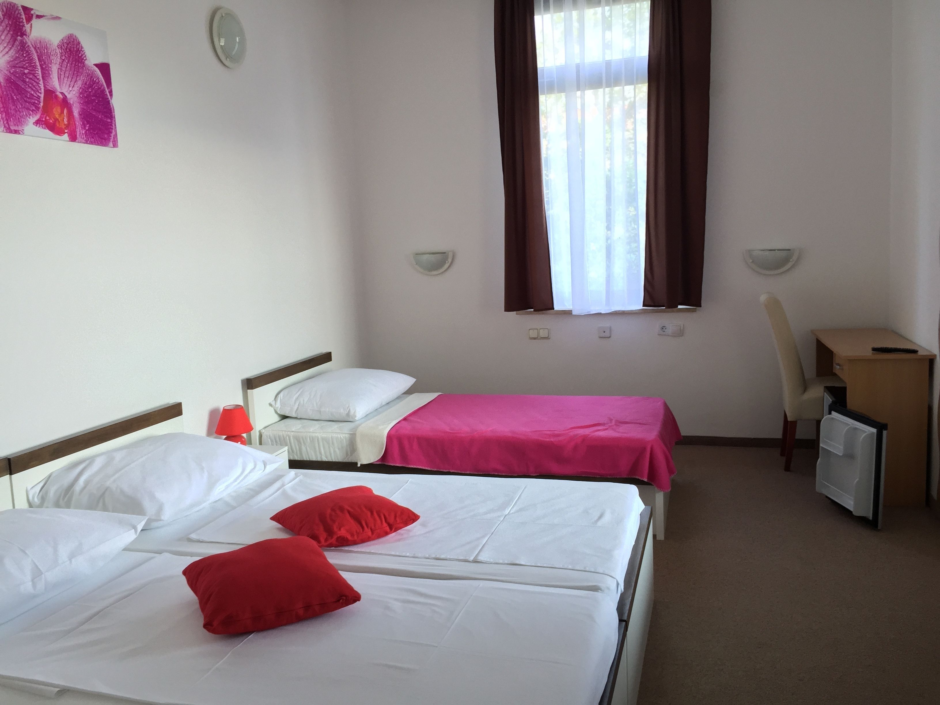 A hotel room with two beds, a desk, a chair, and a window with curtains.