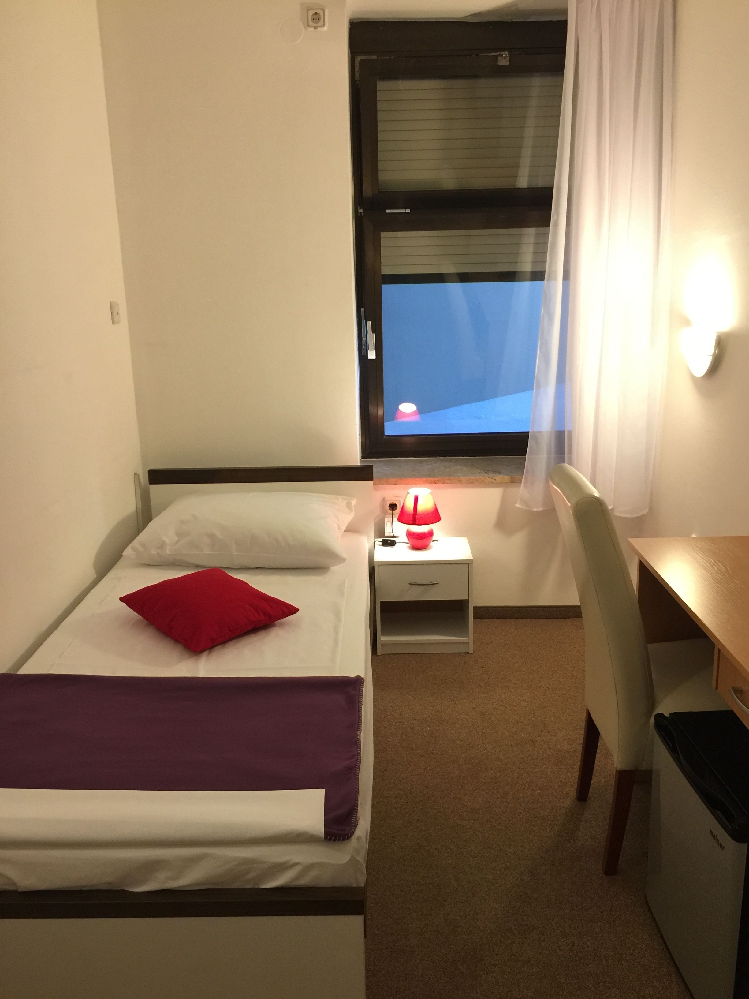 Una camera d'albergo piccola e ordinata, con un letto, una scrivania e una sedia.