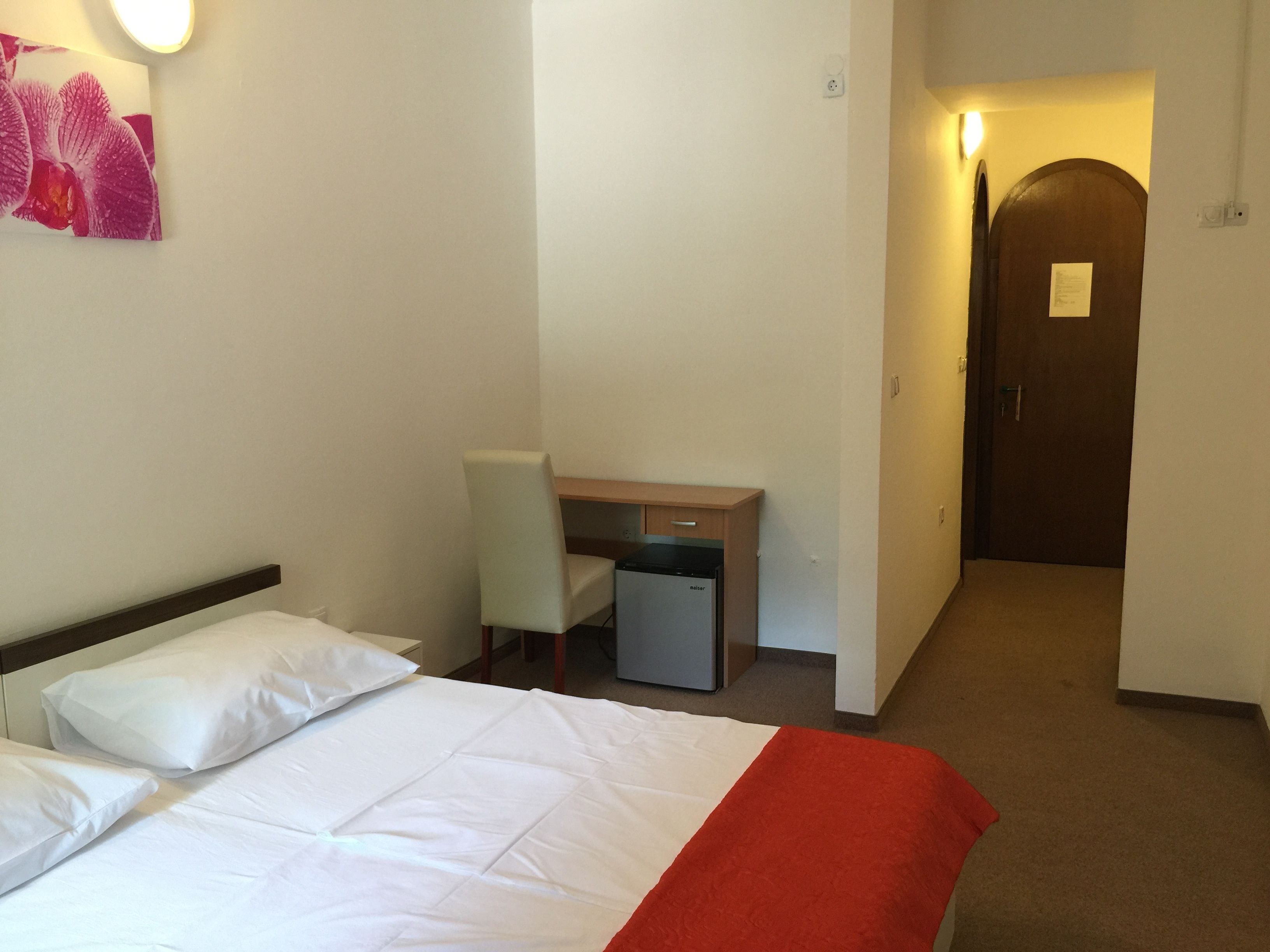 A hotel room with a bed, a desk, a chair, and a small refrigerator.