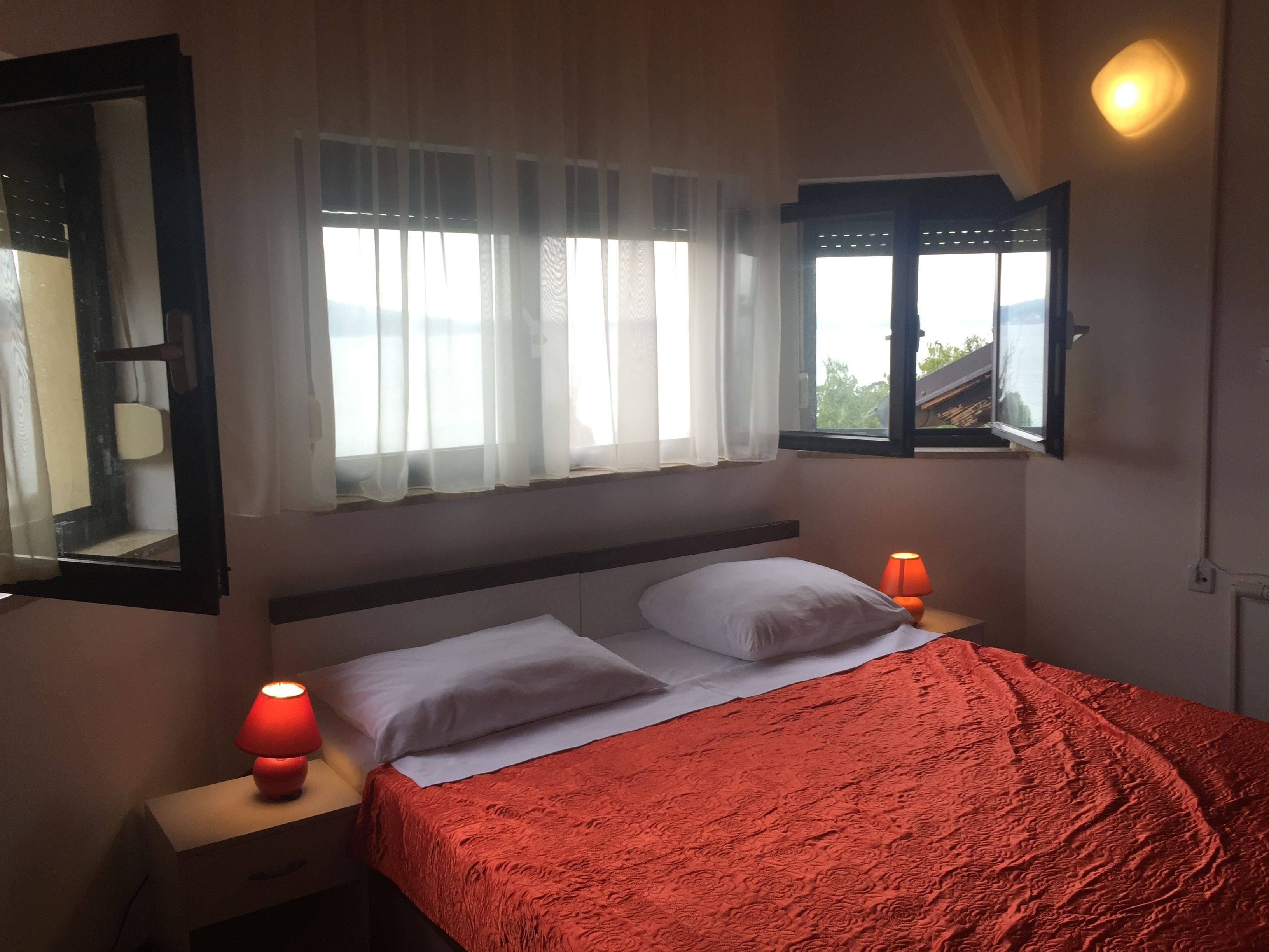 Ein Schlafzimmer mit einem Bett, zwei Nachttischlampen, einem Fenster mit Vorhängen und einem Spiegel an der Wand.